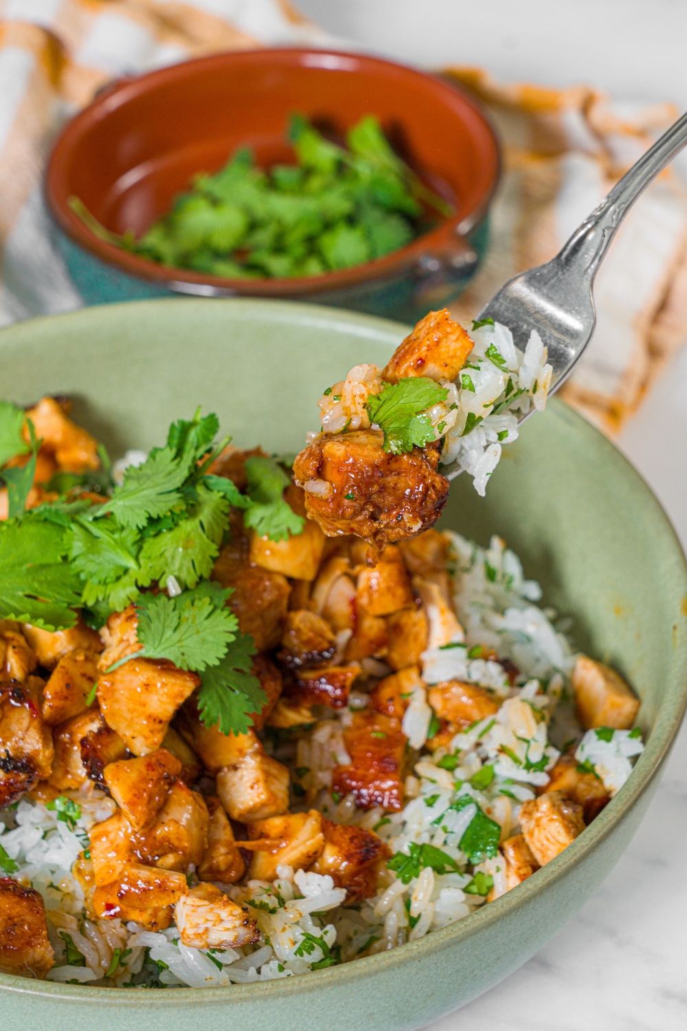 A fork with chipotle honey chicken and cilantro lime rice on it being held over a bowl with the chicken and rice in it.