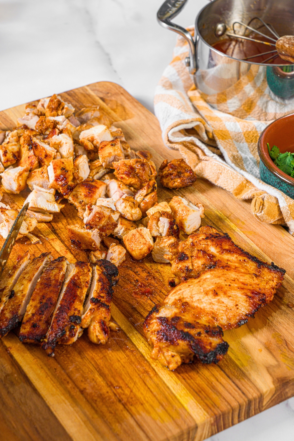 A piece of chipotle honey chicken thigh with a sliced piece next to it and a bunch of pieces of chopped chicken behind it.