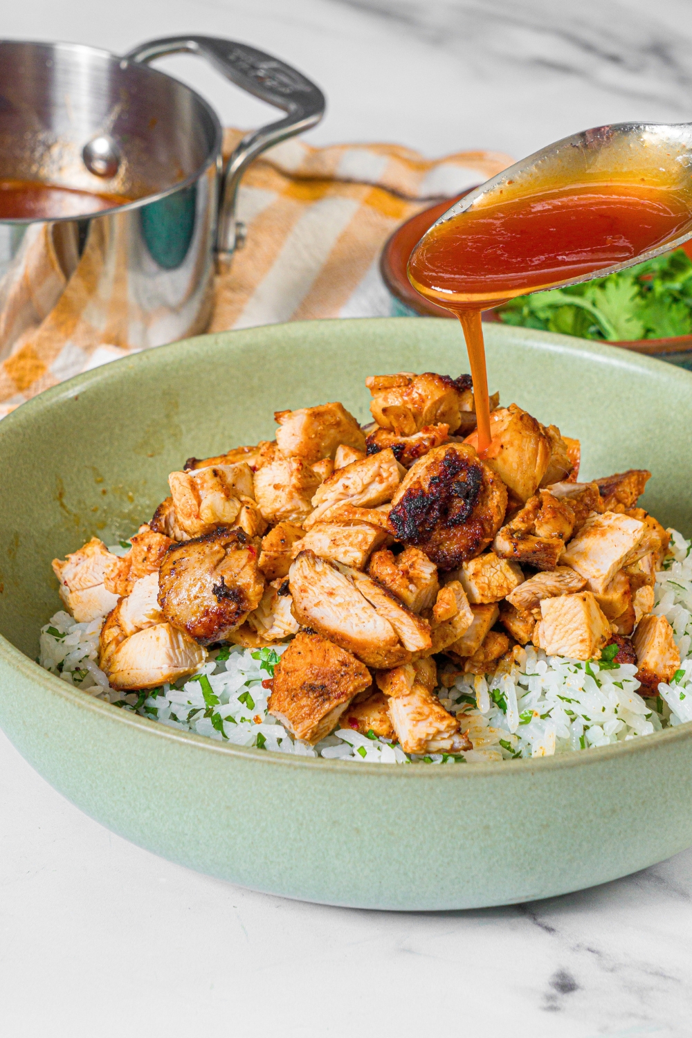 A spoon with chipotle honey sauce drizzling the sauce on top of chipotle honey chicken pieces on top of cilantro lime rice in a bowl.