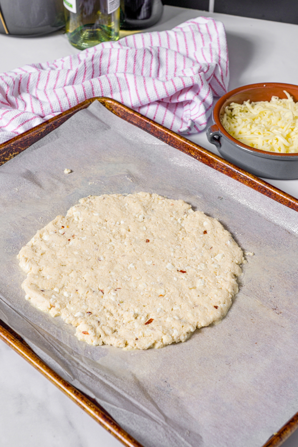 A cottage cheese pizza crust flattened on a sheet of parchment paper on a baking tray.