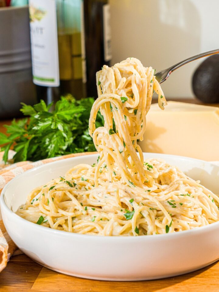 A fork twirled with creamy garlic parmesan pasta noodles being pulled from a bowl that is filled with the garlic parmesan pasta.