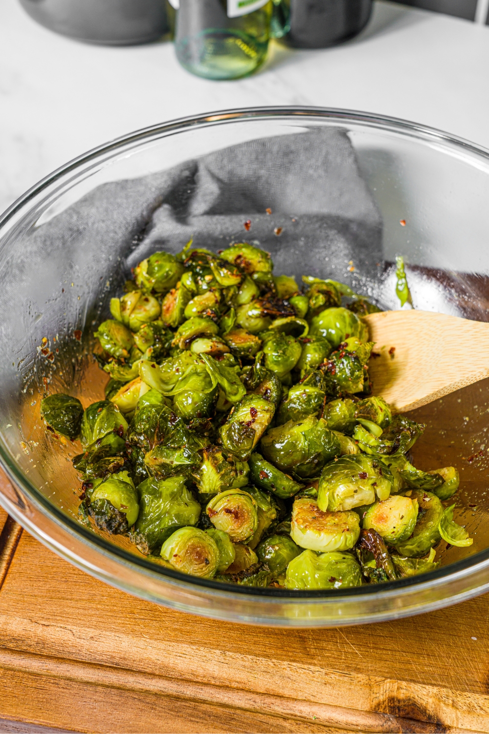Crispy sweet and spicy glazed brussels sprouts in a glass bowl with a wooden spoon mixing them.