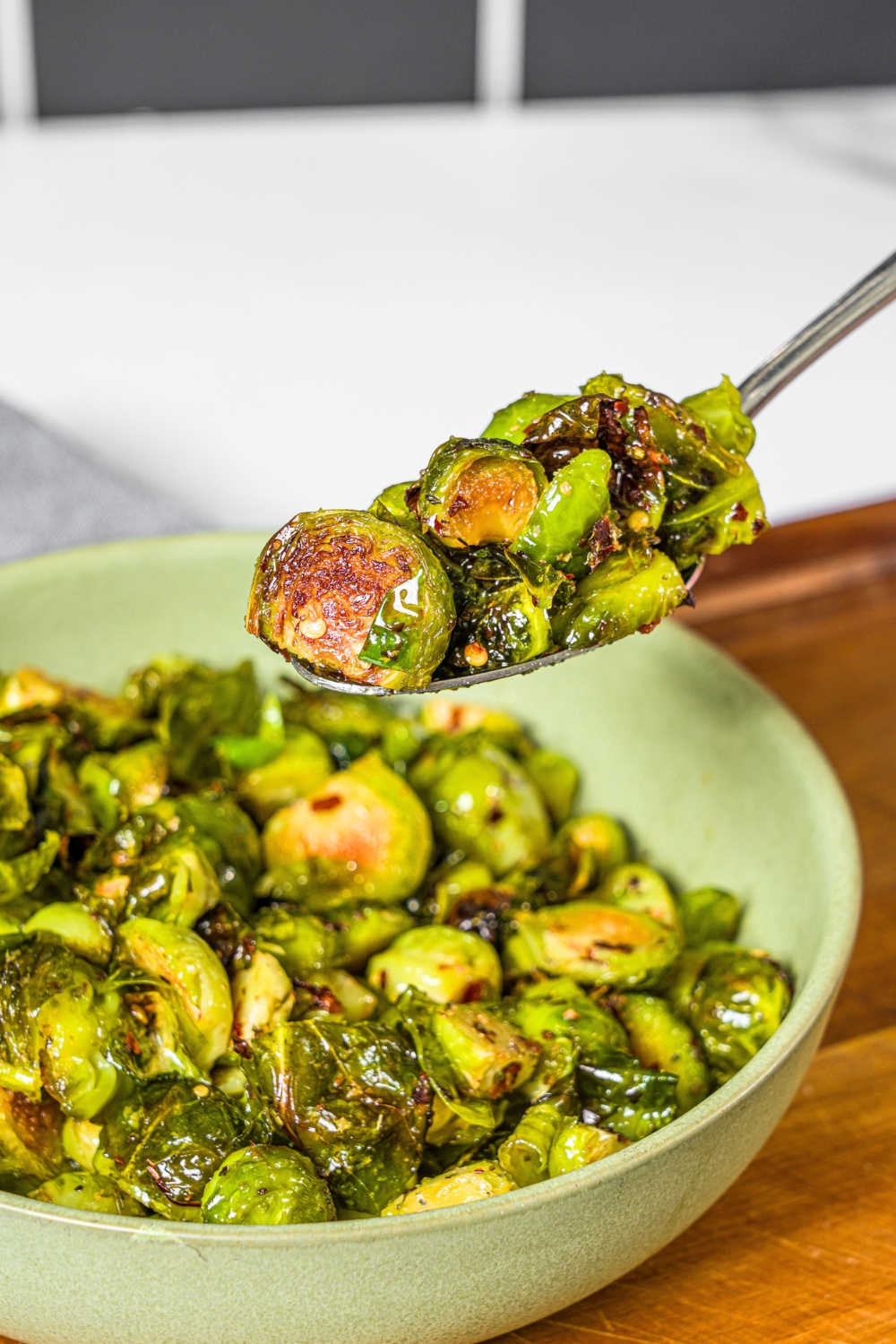 A spoon with crispy brussel sprouts on it being held above a bowl filled with the crispy brussel sprouts.