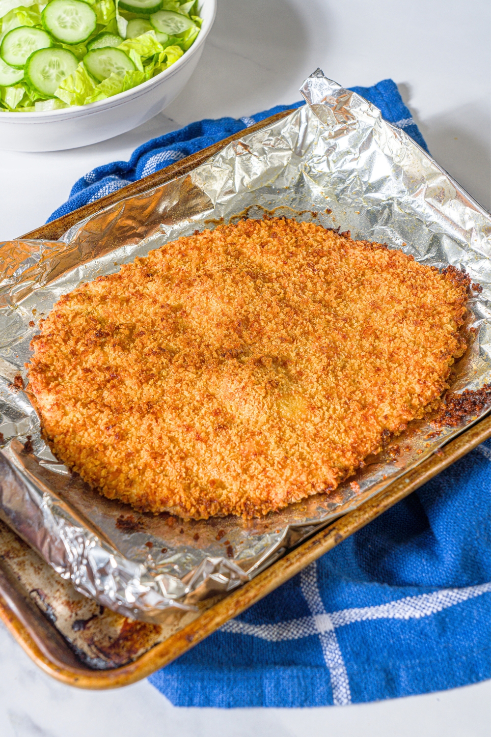 A giant crispy ground chicken cutlet on a sheet of aluminum foil on a baking sheet.