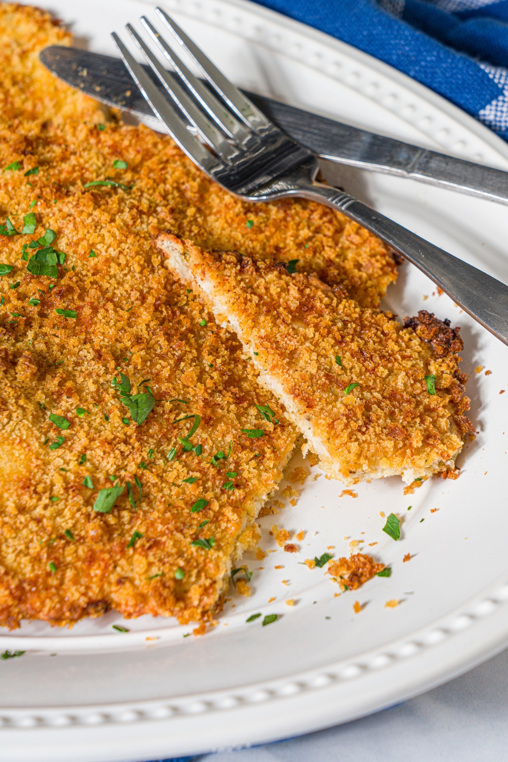 A slice of a ground chicken cutlet on top of the giant oven baked ground chicken cutlet on a white plate.