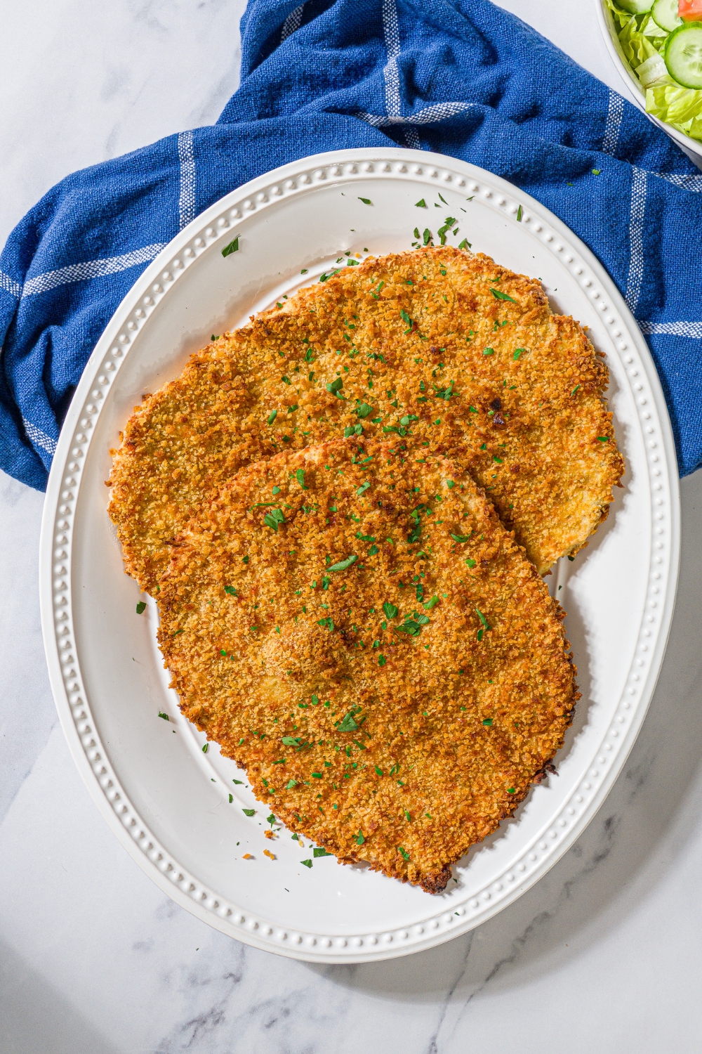 Two giant ground chicken cutlets, overlapping one another on a white plate.