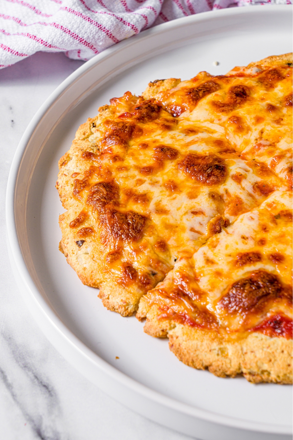Part of a white plate that has half of a cheese protein pizza on it.