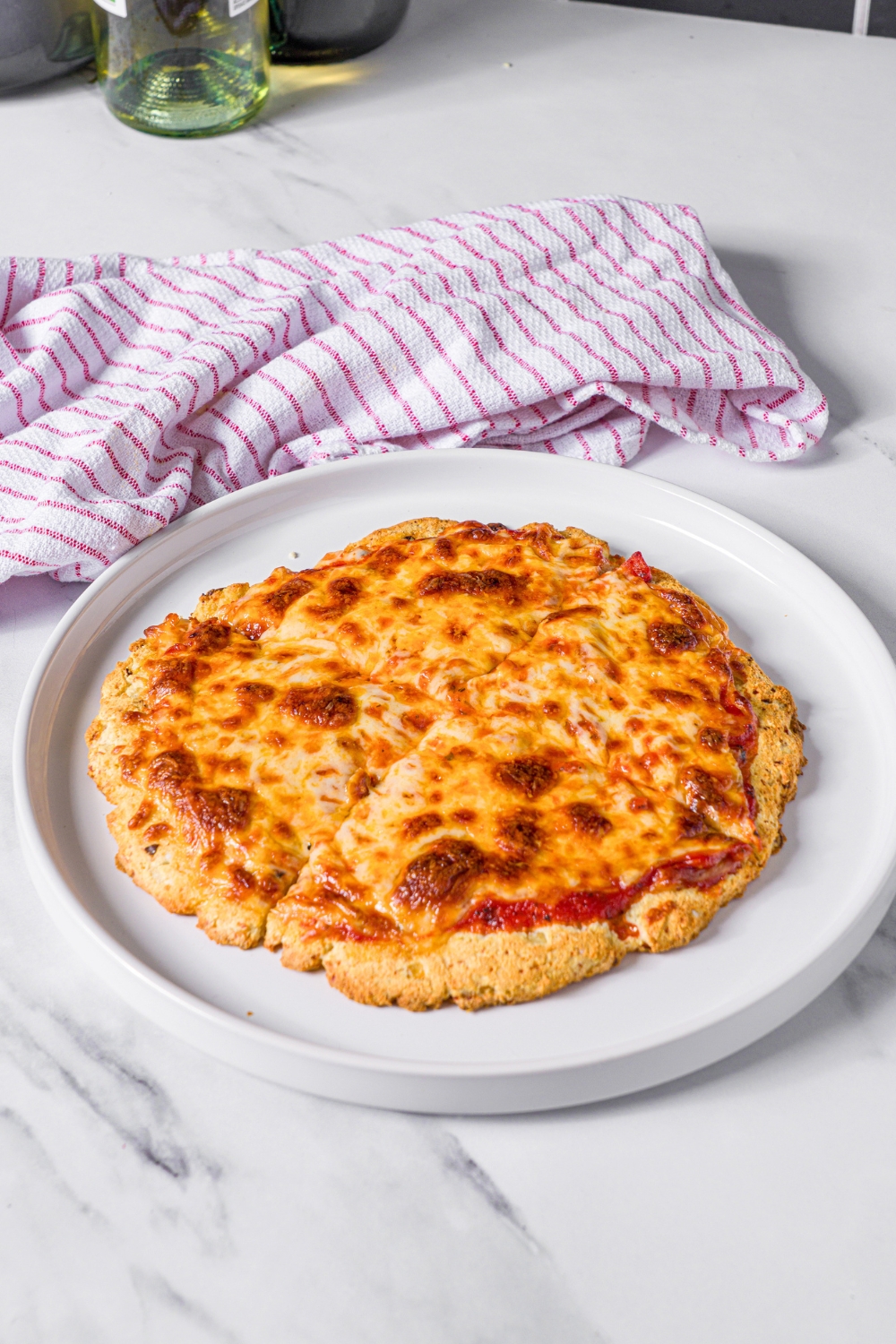 A cheese, high protein pizza sliced in four slices on a white plate.