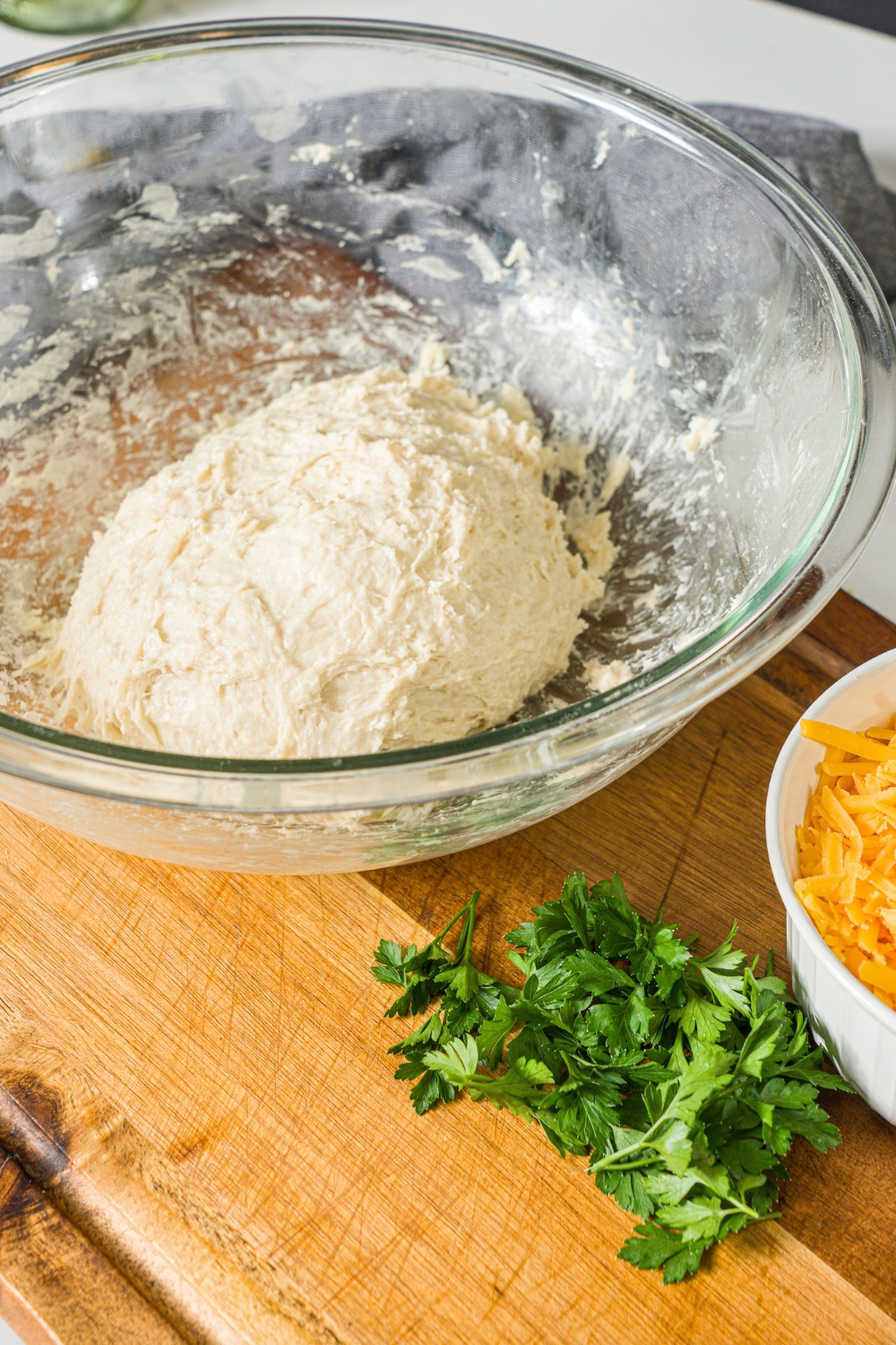 A glass bowl with a ball of bread dough. The bowl is on a wooden counter.