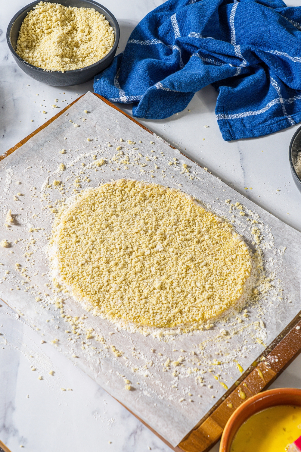 A giant breaded uncooked ground chicken cutlet on a flowered sheet of parchment paper on a baking tray.