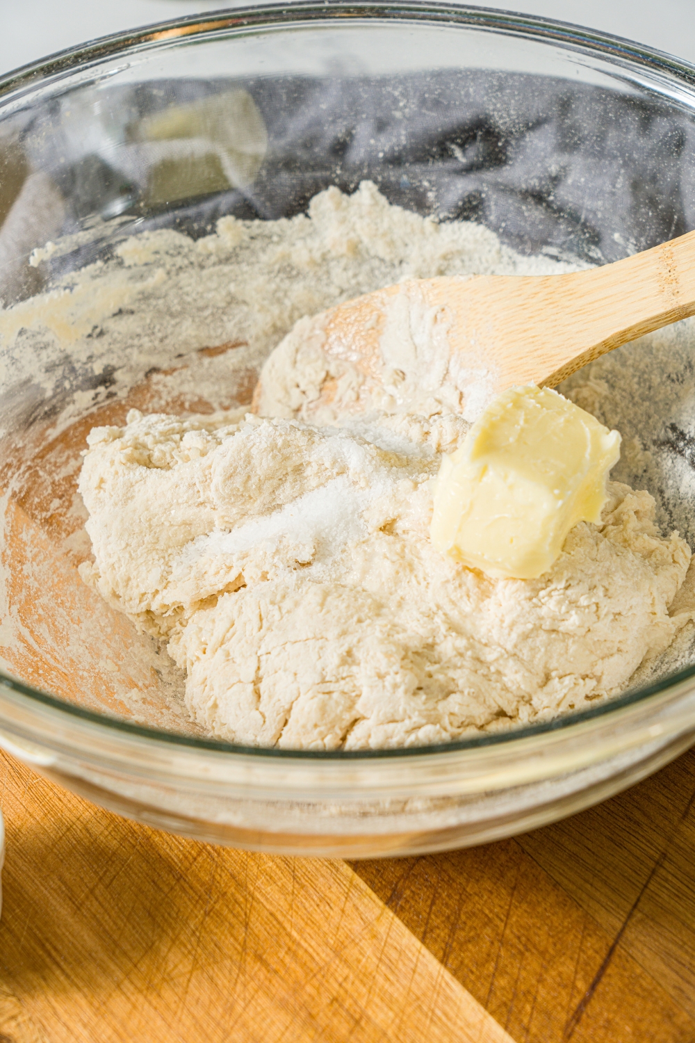 A glass bowl with a wooden spoon mixing ingredients to make pull apart cheesy garlic bread including flour, butter, yeast, and sugar.