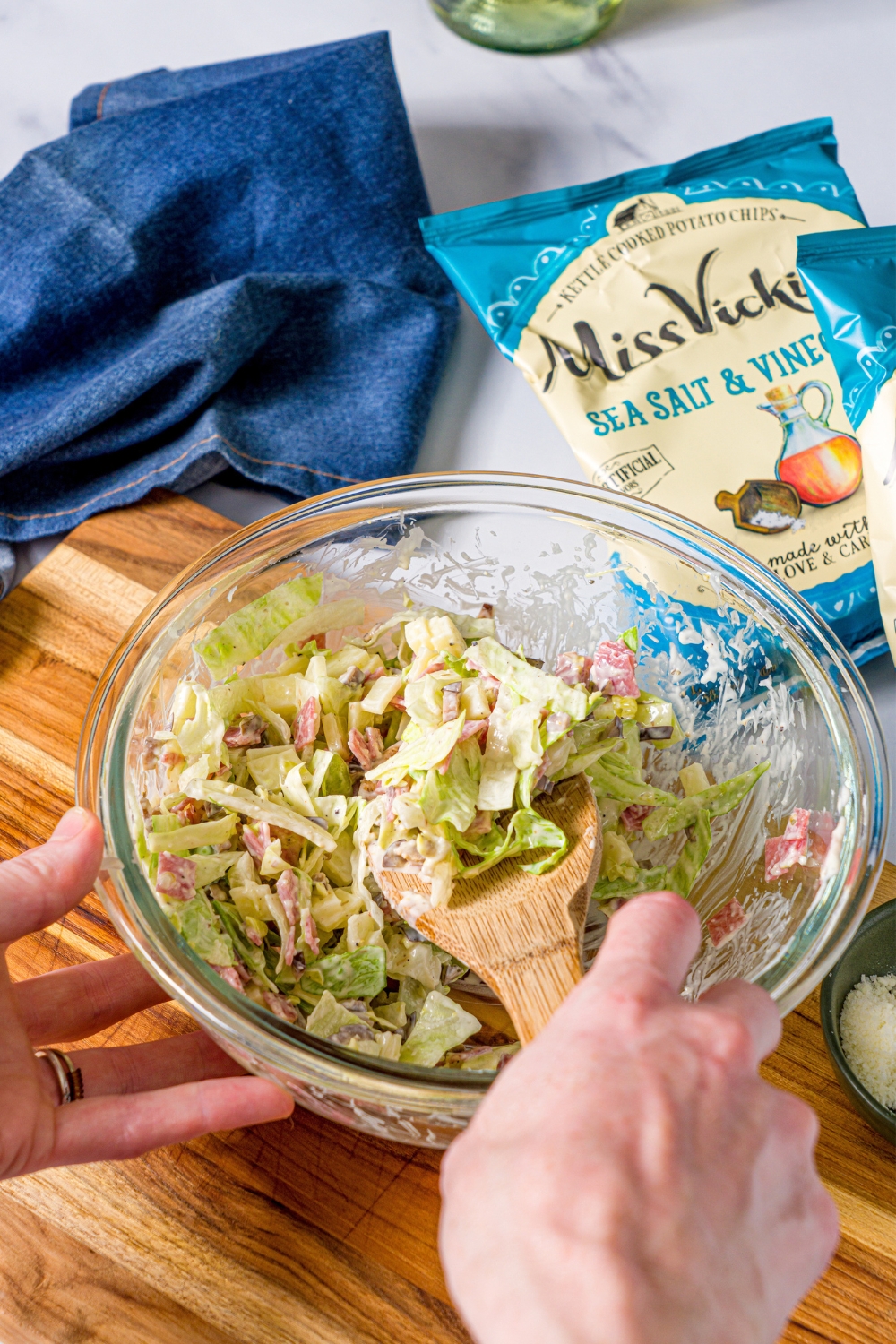 A hand with a wooden spoon, mixing together a chopped Italian sandwich filling.