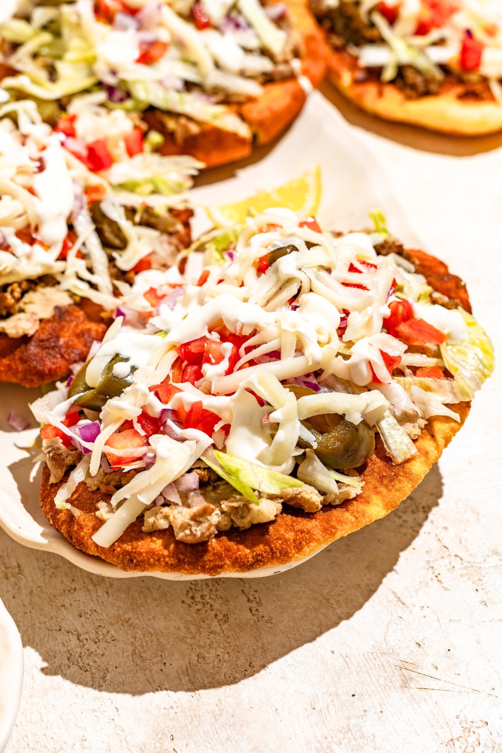 An Indian taco that has ground beef, shredded cheese, jalapenos, tomatoes, lettuce, onion, and a white sauce on top of Indian fry bread.