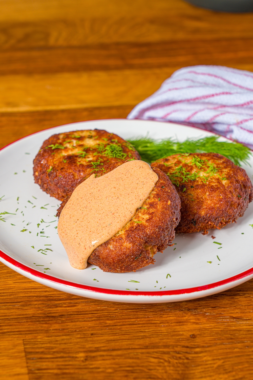 Three crab cakes on a white plate. The front crab cake has a crab cake sauce on top of it.