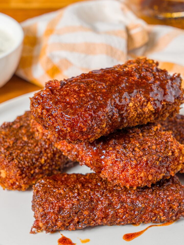 A stack of four Nashville hot mozzarella sticks on a white plate.