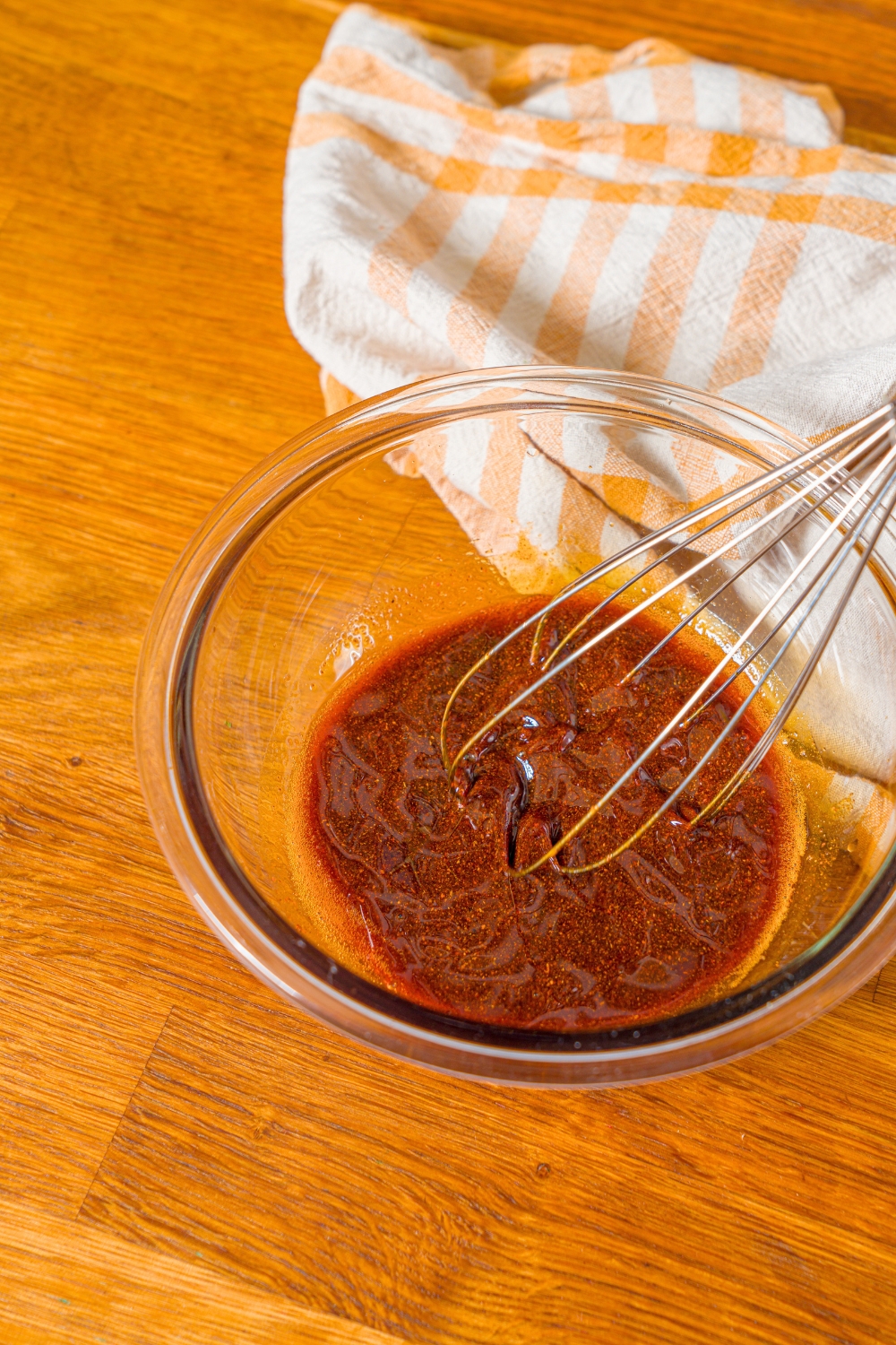 A whisk in a glass bowl that's filled with Nashville hot sauce.