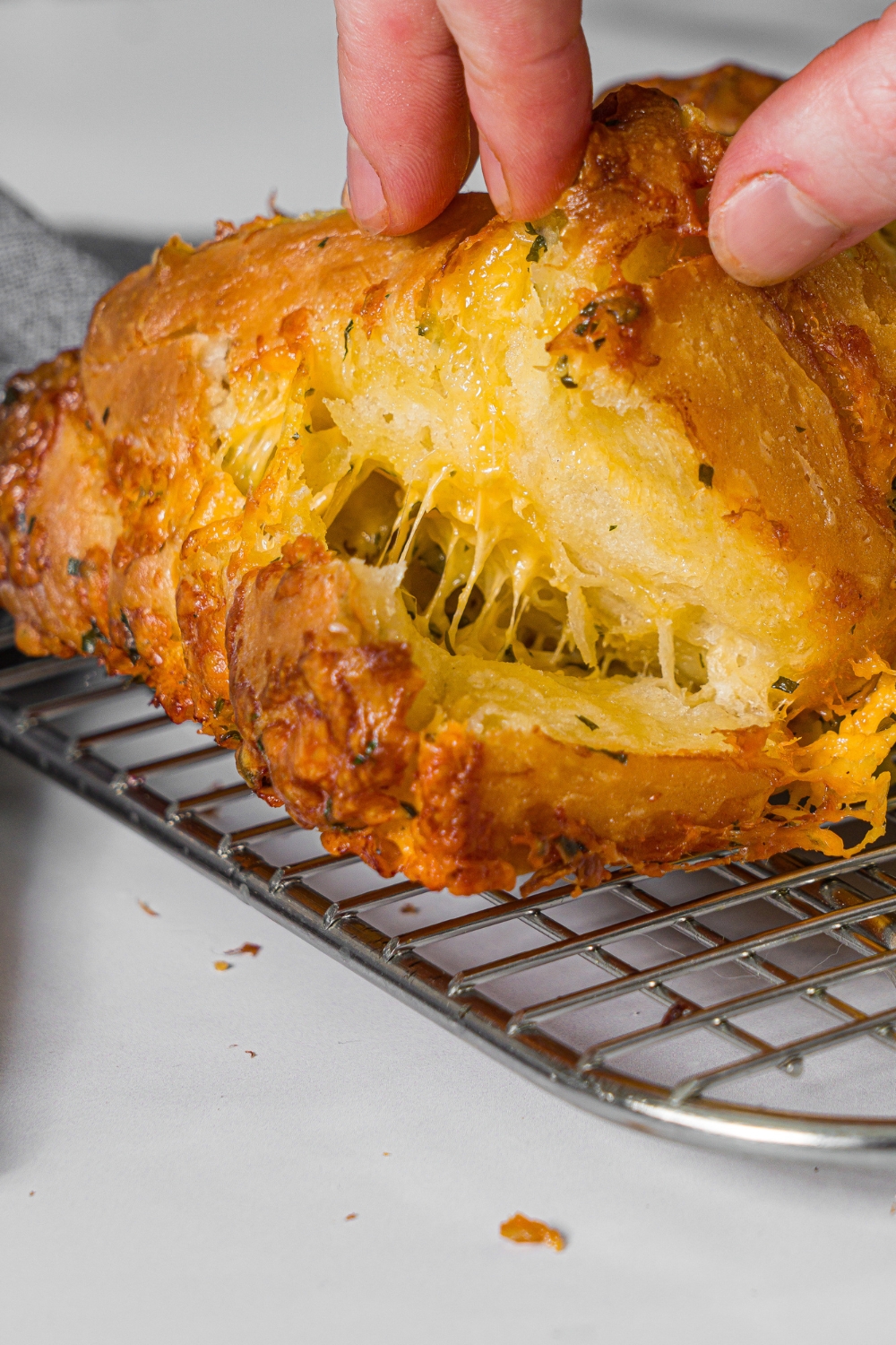 A wire rack with a loaf of pull apart garlic bread. A hand is pulling up a piece of bread.