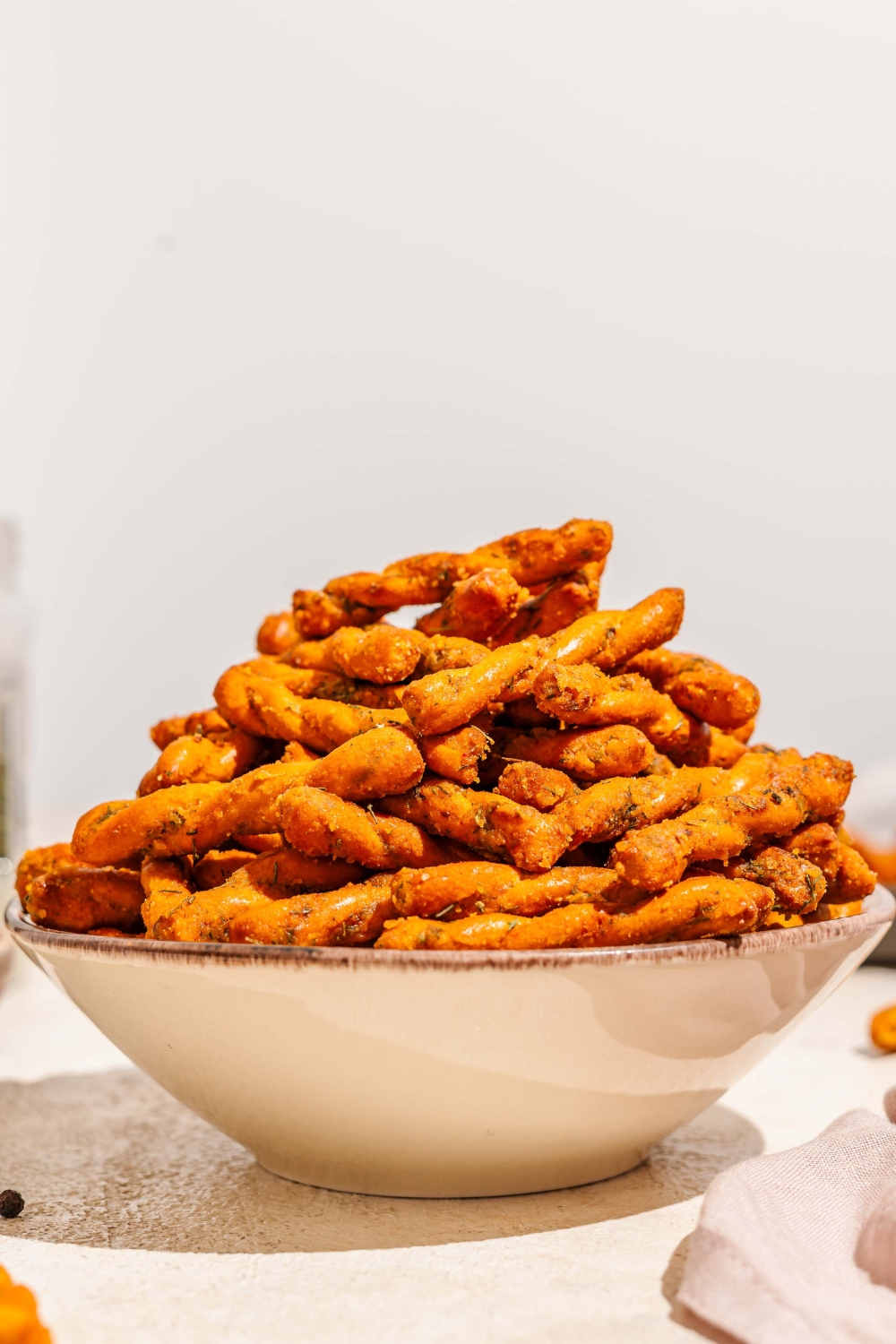 A bowl of seasoned pretzel braids. The bowl is on a tan counter with a white cloth napkin.