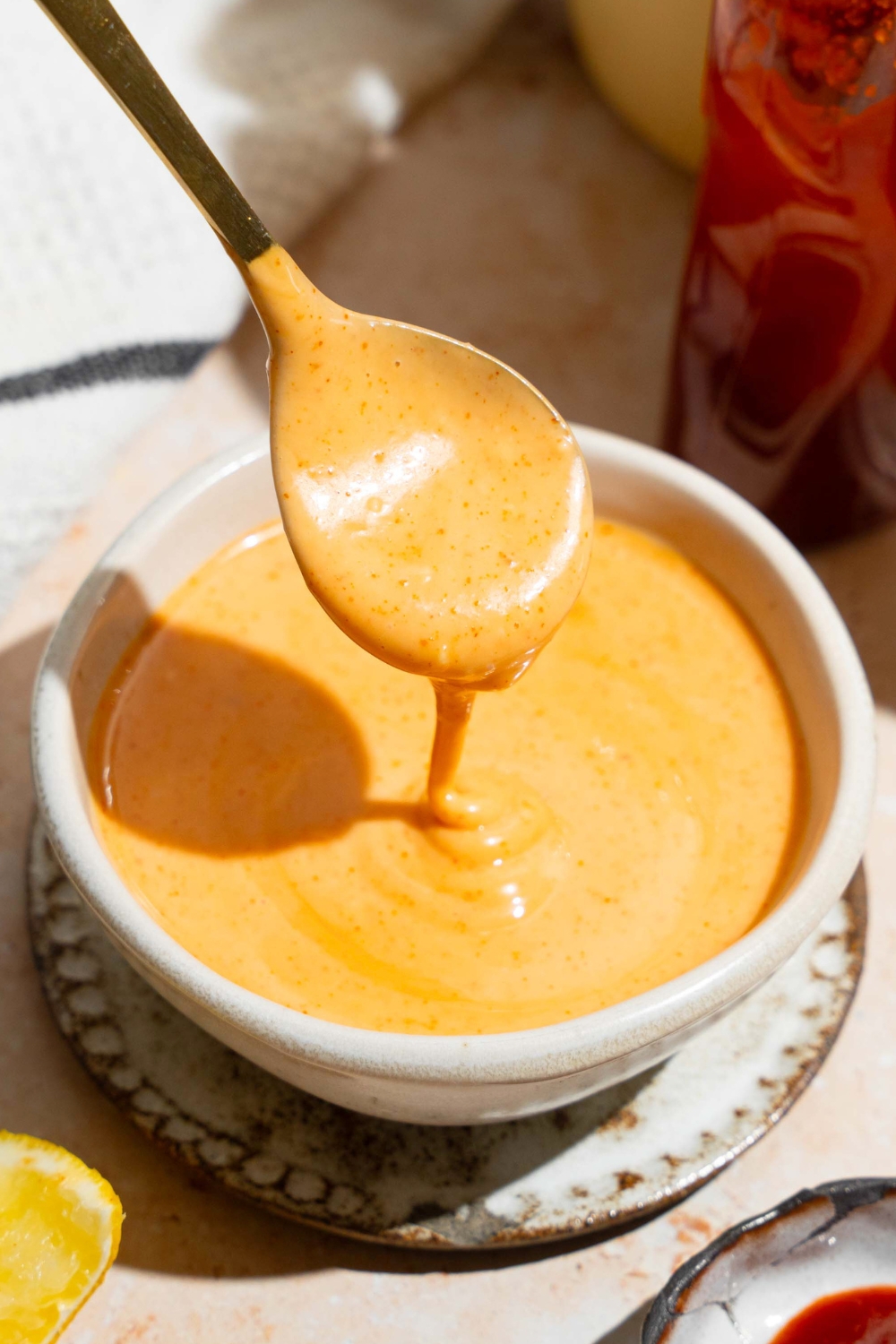 A spoon with honey sriracha sauce on it drizzling the sauce into a white bowl that is filled with the sauce.