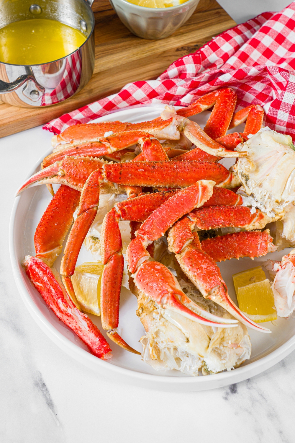A bunch of steamed crab legs on a white plate with lemon wedges. Behind the plate is a pot of melted butter.
