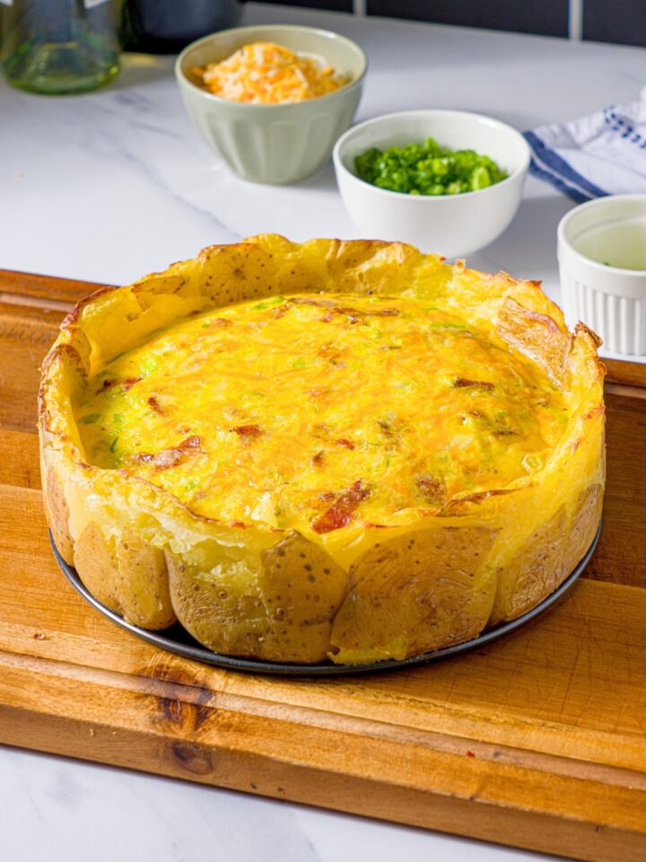 A potato crust quiche with a cheesy, egg bacon filling on a wooden cutting board.