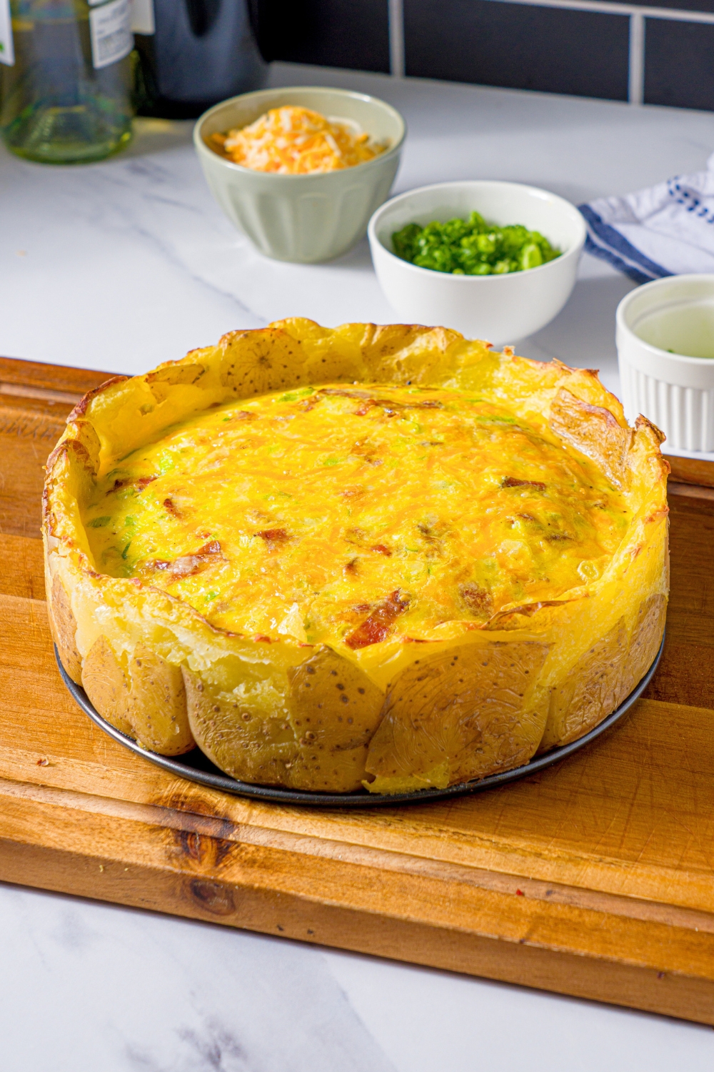 A potato crust quiche with a cheesy, egg bacon filling on a wooden cutting board.