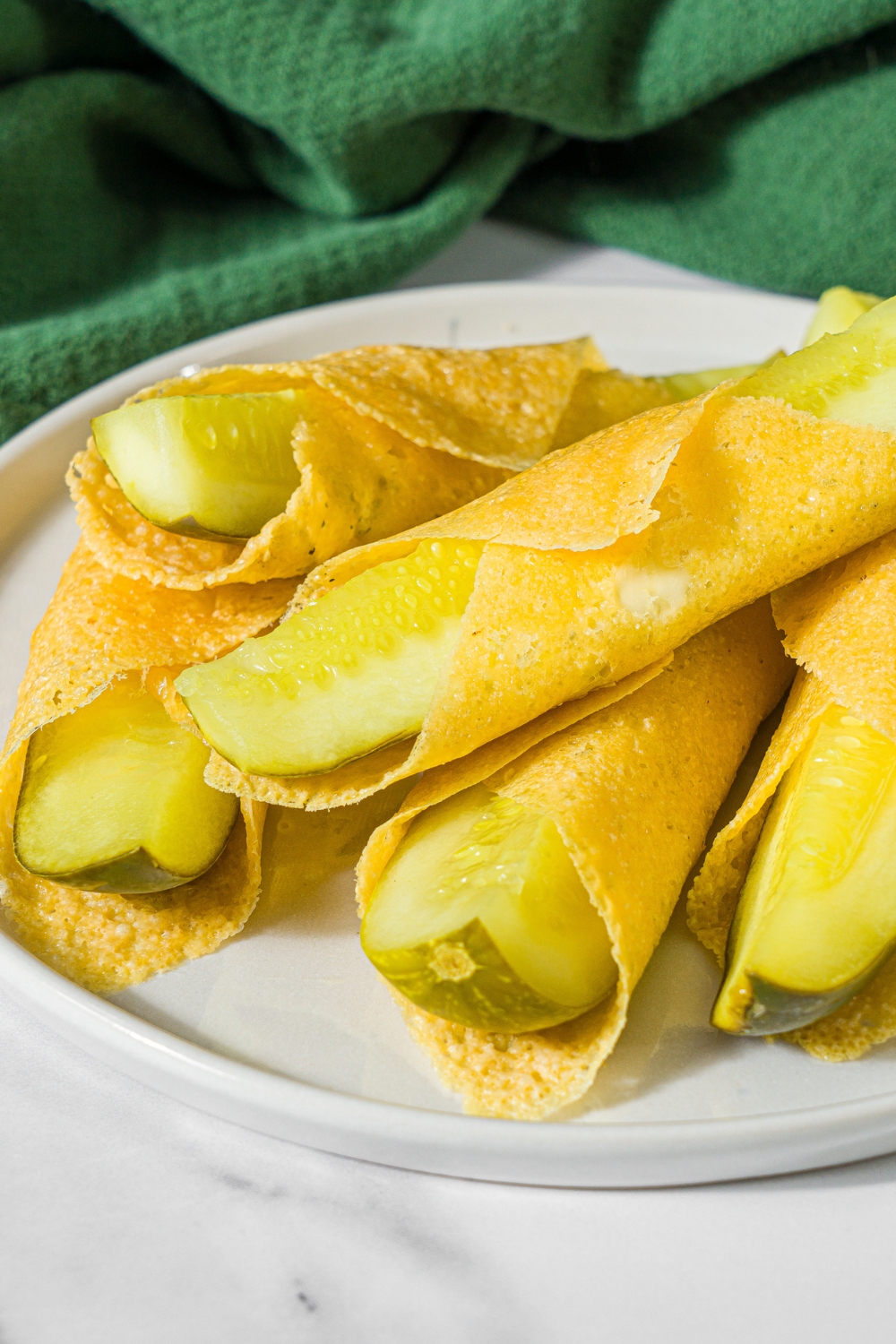 A plate with a pile of chickles made with pickles and cheese. The plate is on a marble counter with a green cloth napkin.