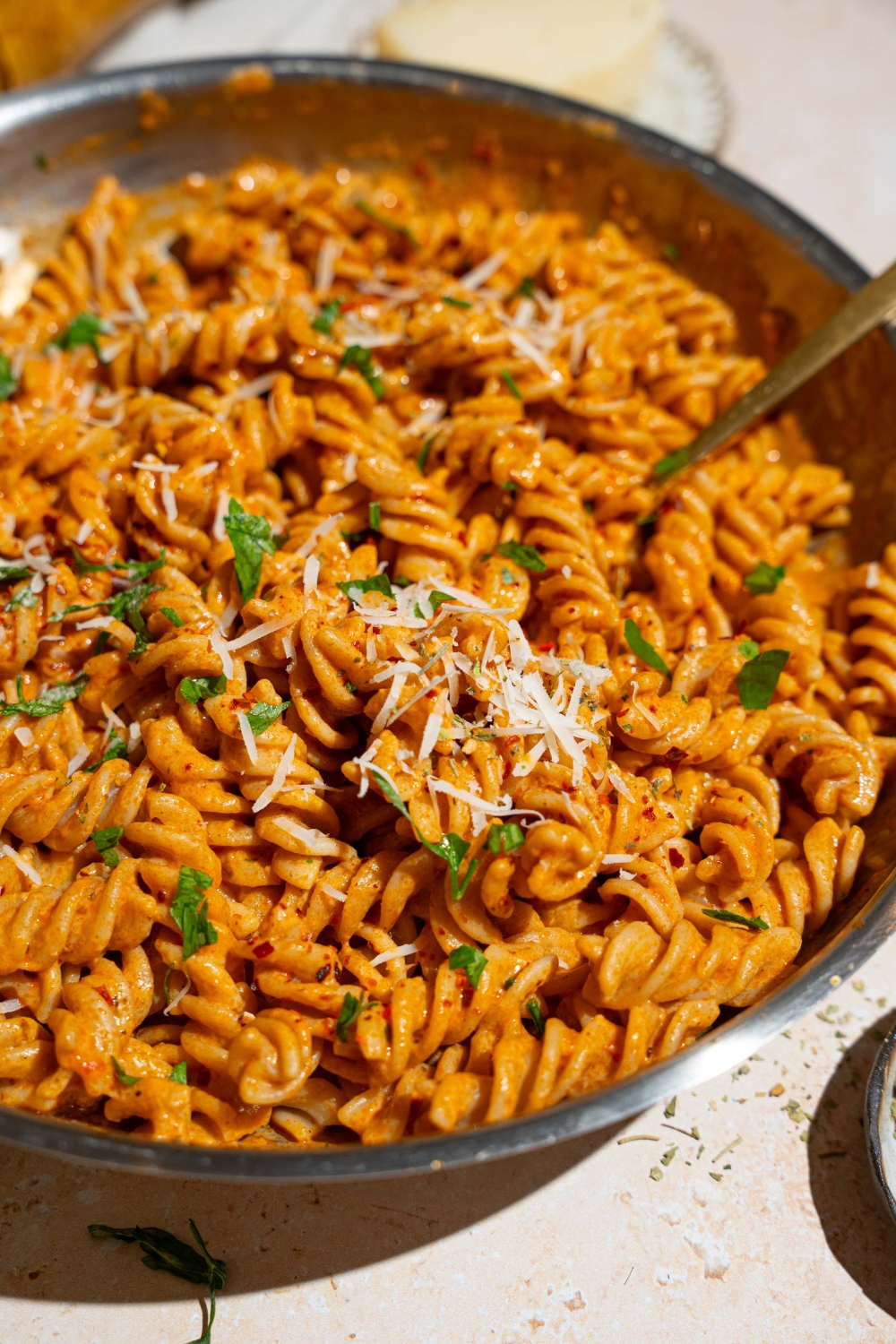 A skillet with fusilli pasta tossed in creamy tomato pasta sauce garnished with fresh basil and shredded cheese. There is a fork in the pasta.