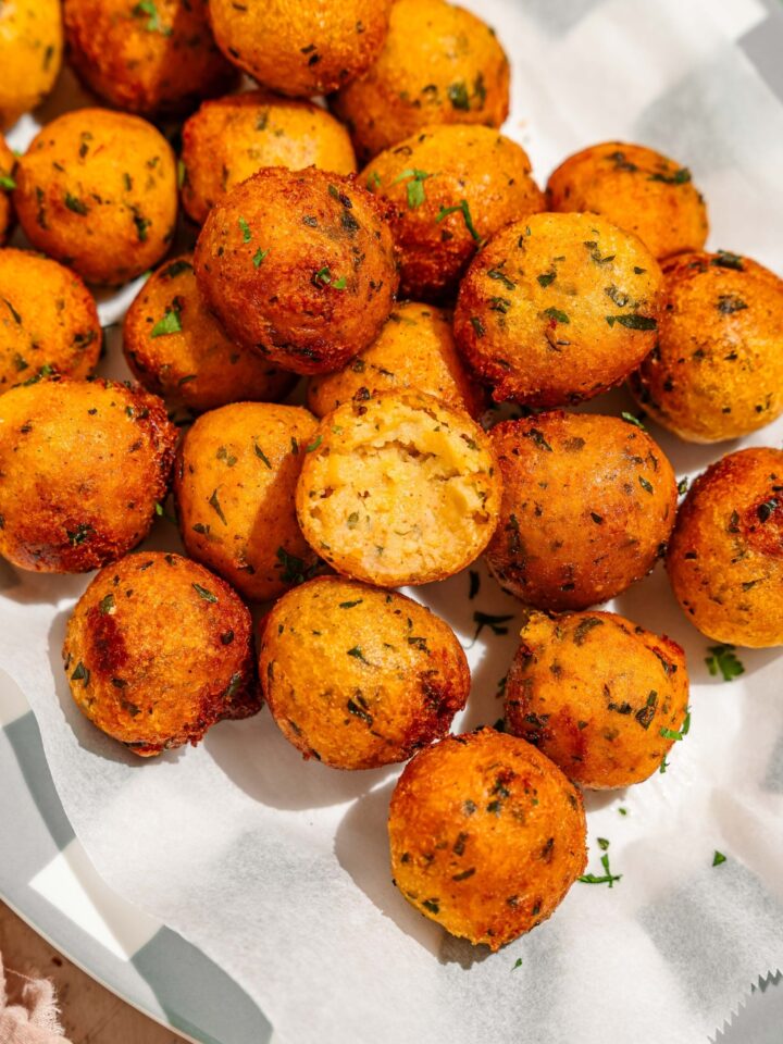 A platter lined with parchment paper with crispy potato balls garnished with fresh parsley.