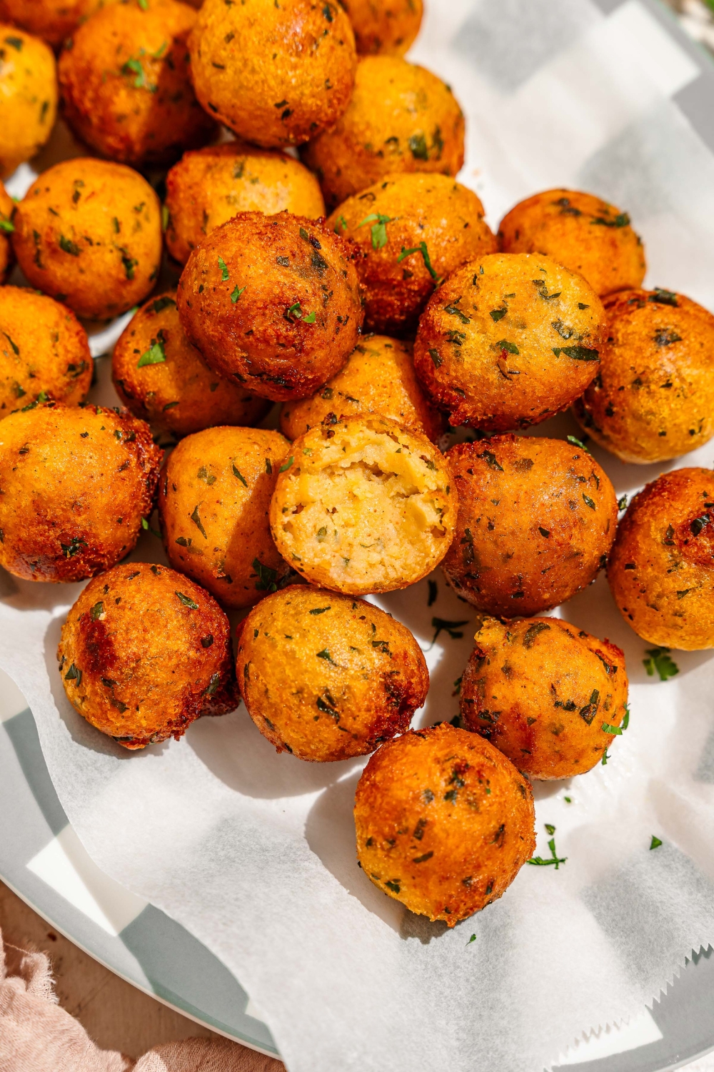 A platter lined with parchment paper with crispy potato balls garnished with fresh parsley.