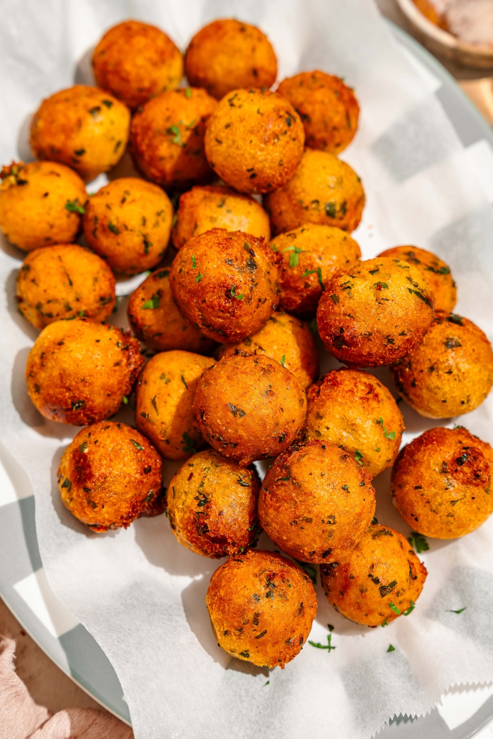 A platter lined with parchment paper with crispy potato balls garnished with fresh parsley.