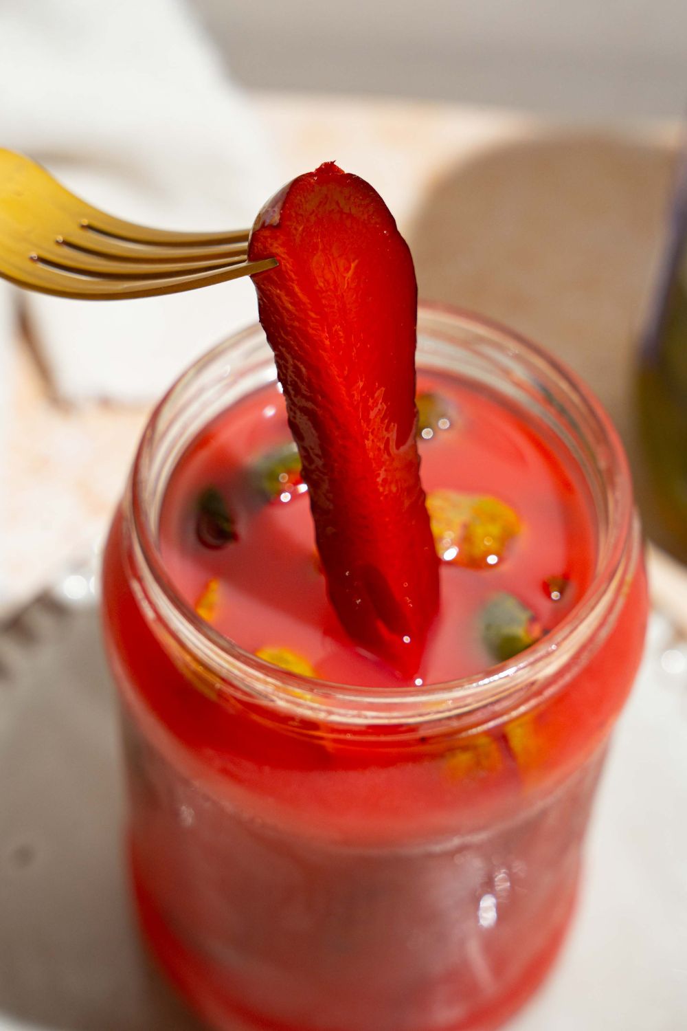 A jar of kool aid pickles with a fork pulling a pickle from the jar. The jar is on a tan counter.
