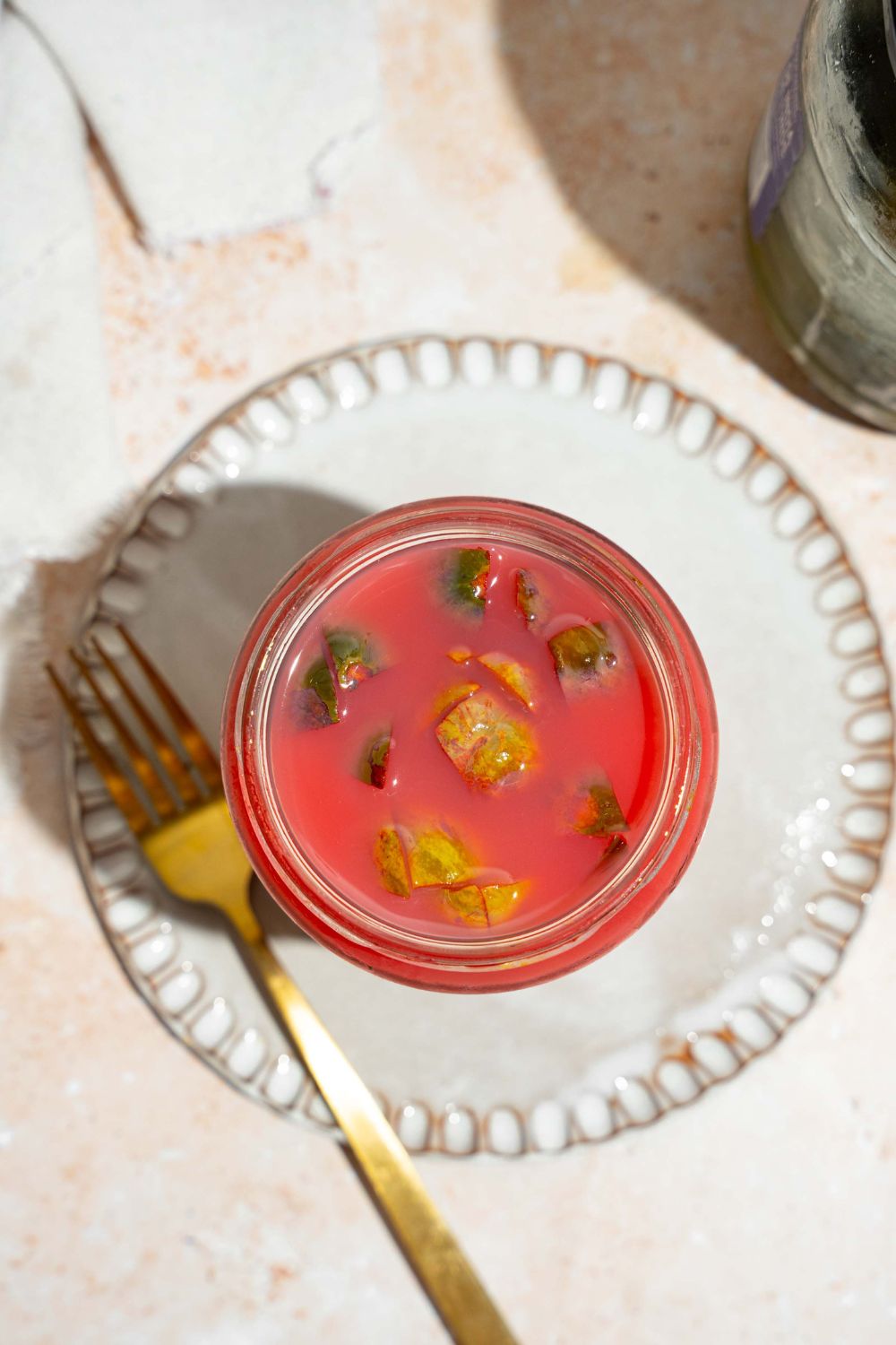 A jar of kool aid pickles on a white plate. The plate is on a tan counter and served with a fork.