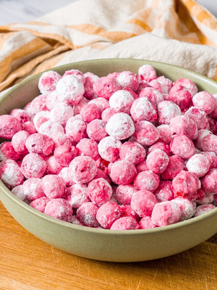A green bowl with candied cranberries on a wooden board with a yellow striped napkin.