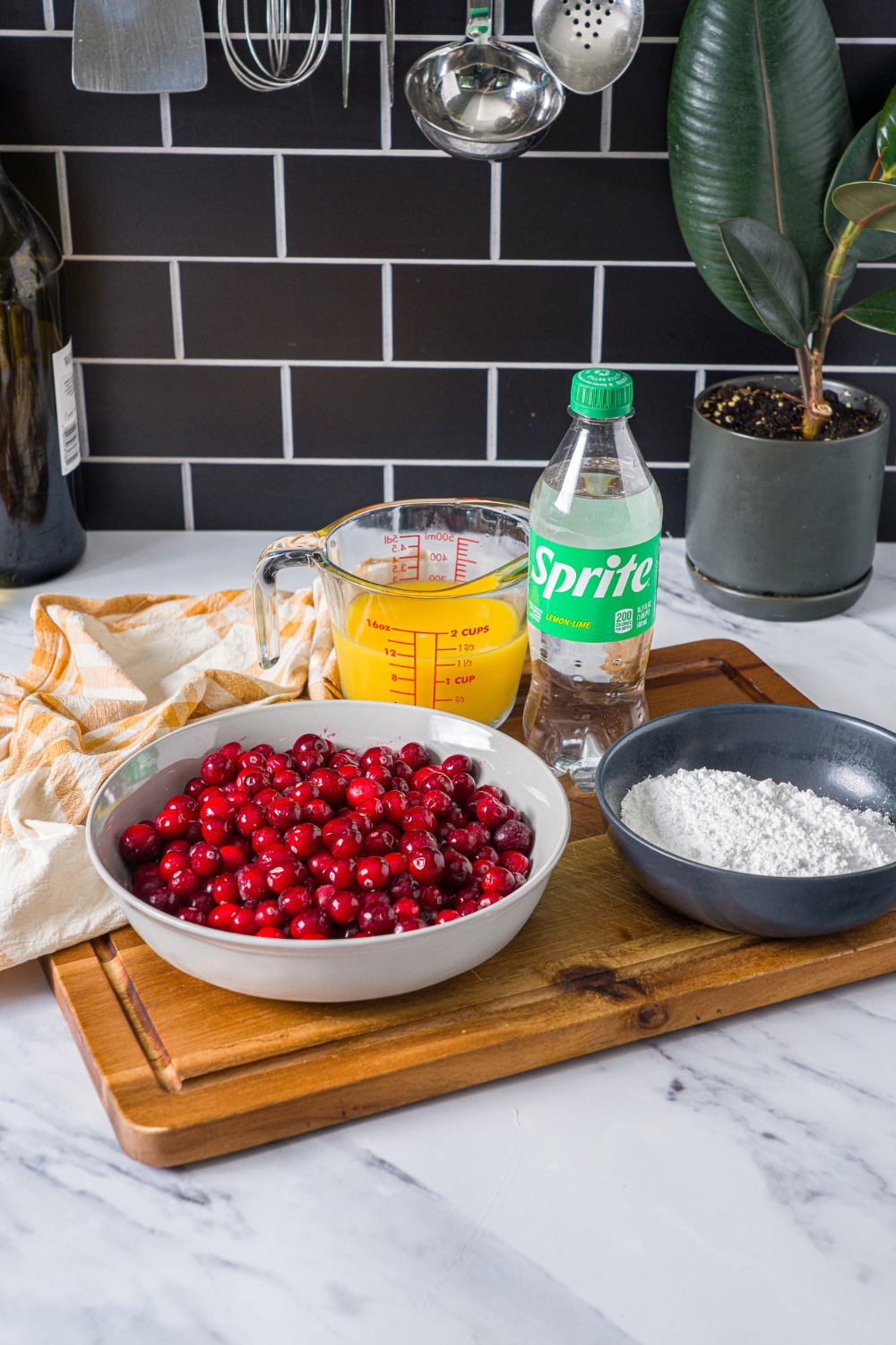 A wooden board with ingredients to make candied cranberries including cranberries, orange juice, sprite, and sugar.