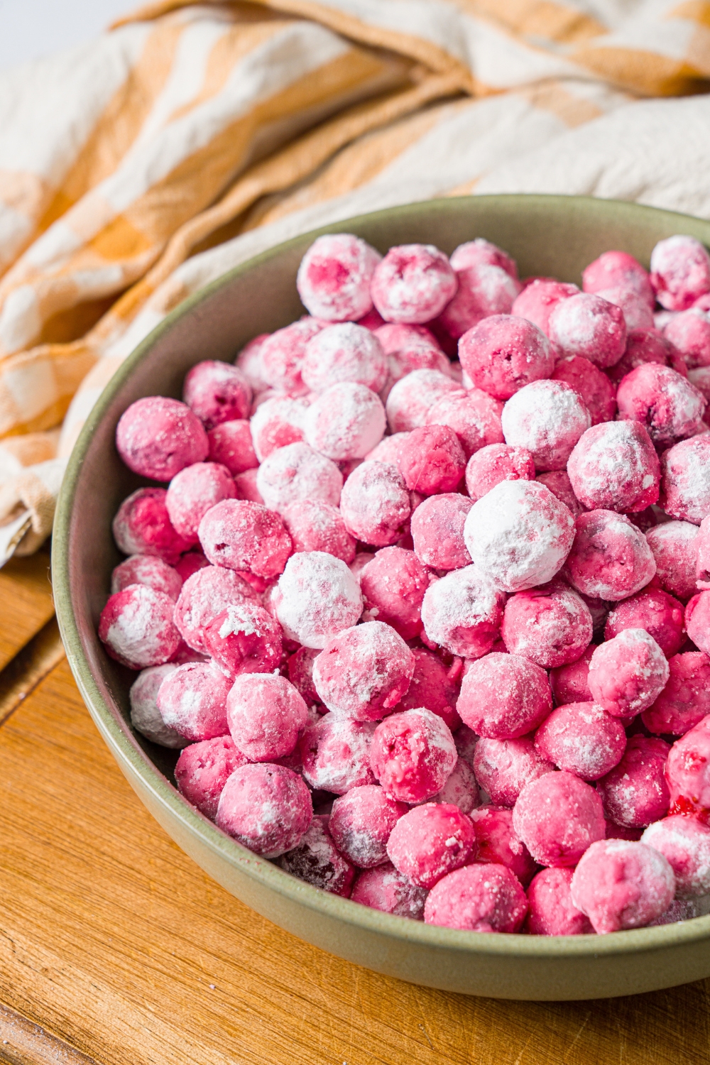 A green bowl with candied cranberries on a wooden board with a yellow striped napkin.