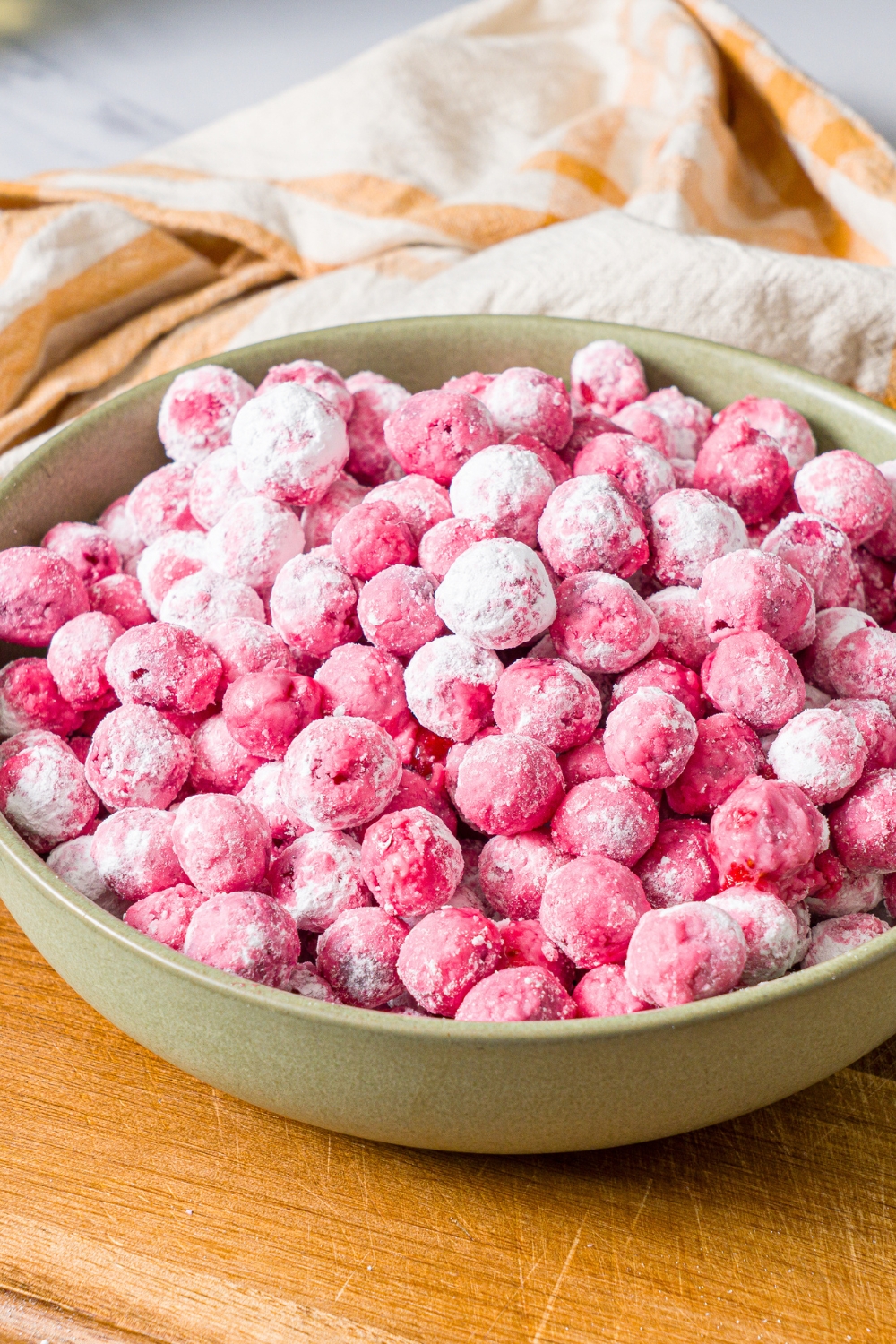 A green bowl with candied cranberries on a wooden board with a yellow striped napkin.