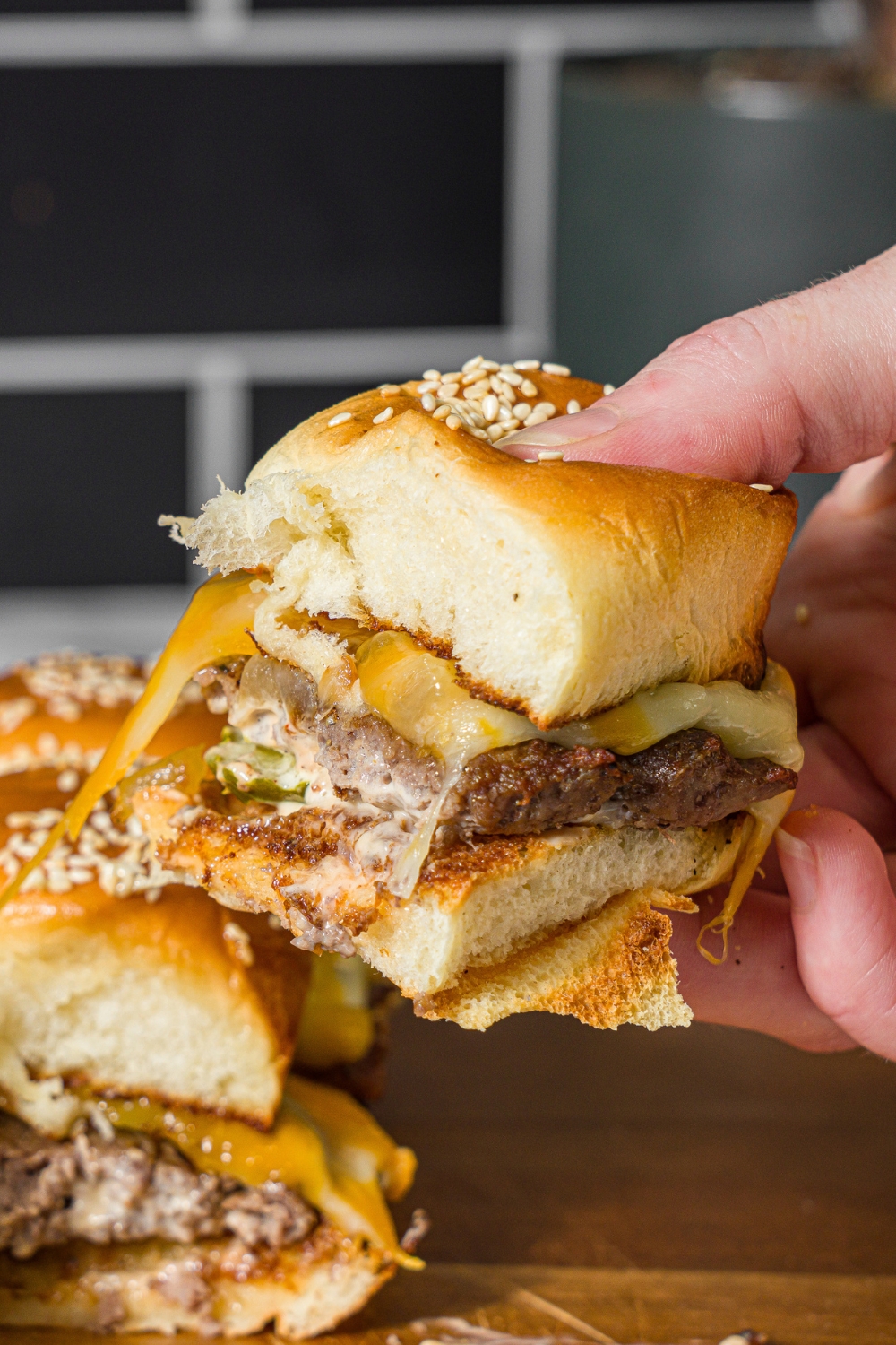 A hand pulling a cheeseburger slider from a set of sliders on a wooden board.