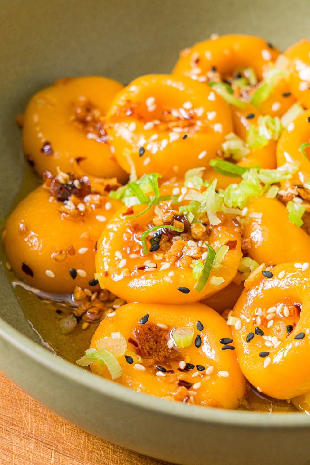 A green bowl with carrot button noodles tossed in a chili crisp sauce and garnished with sliced green onions. The bowl is on a wooden board.