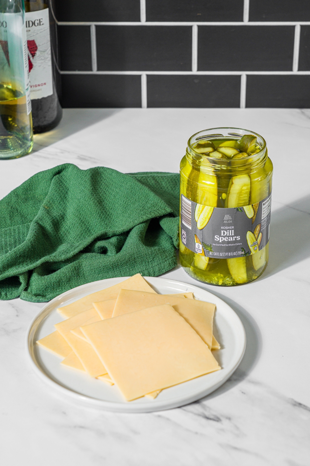 A marble counter with ingredients to make chickles including pickles and slices of gouda cheese.