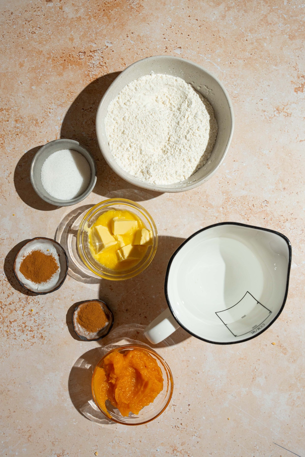 A tan counter with ingredients to make pumpkin cinnamon roll pancakes including pancake mix, pumpkin puree, vanilla extract, butter, water, sugar, and spices.