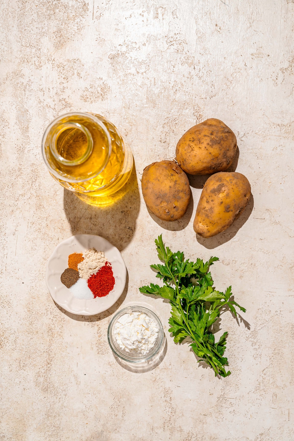 A tan counter with ingredients to make crispy potato balls including potatoes, oil, cornstarch, and seasonings.