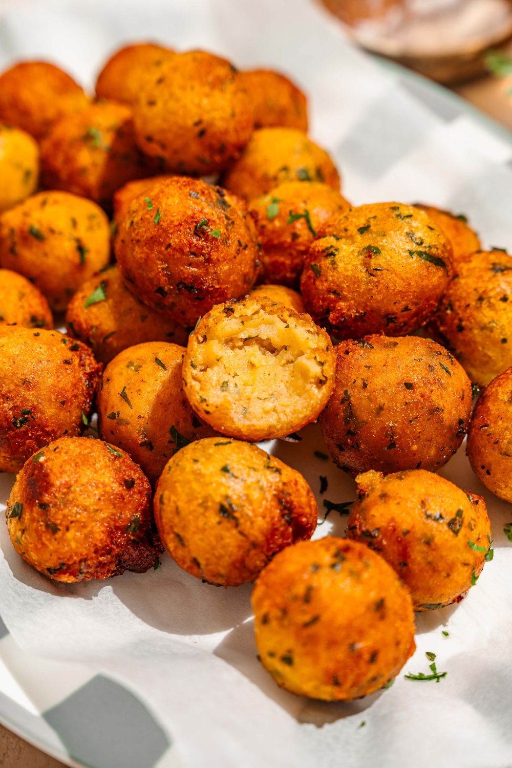 A platter lined with parchment paper with crispy potato balls garnished with fresh parsley. One of the balls has a bite taken from it.