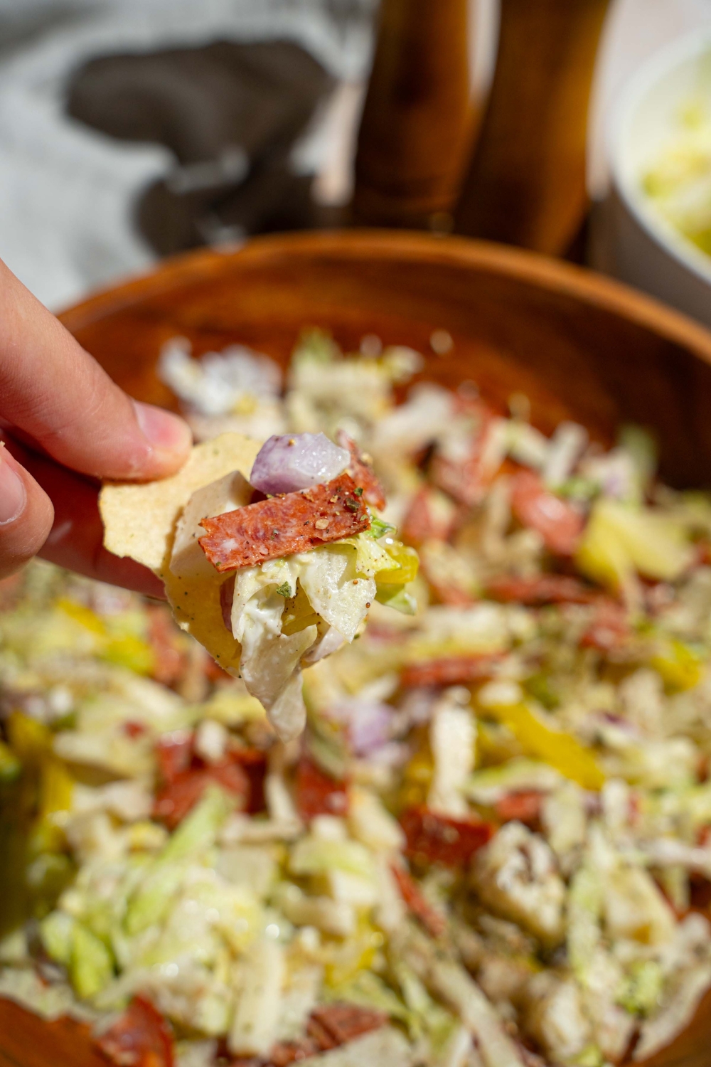 A close up of a chip dipped in Italian grinder dip with a bowl of Italian grinder dip blurred in the background.