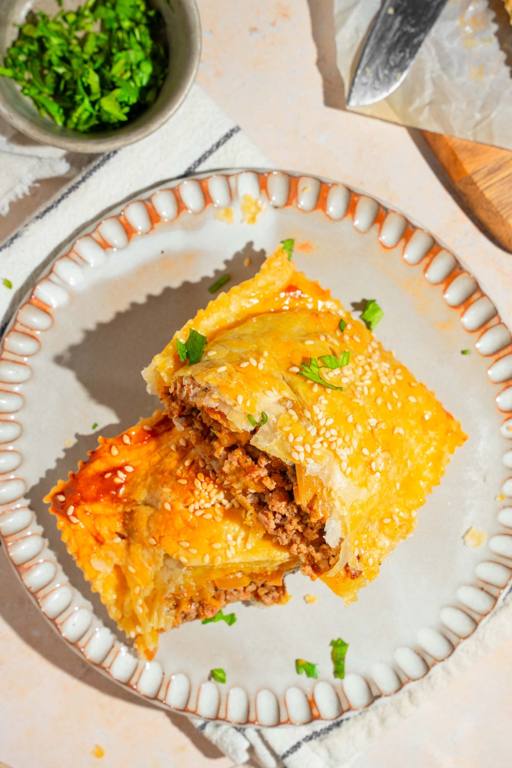 A white plate with a sliced cheeseburger hot pocket garnished with fresh parsley. The plate is on a white striped napkin on a tan counter with a small bowl of parsley.