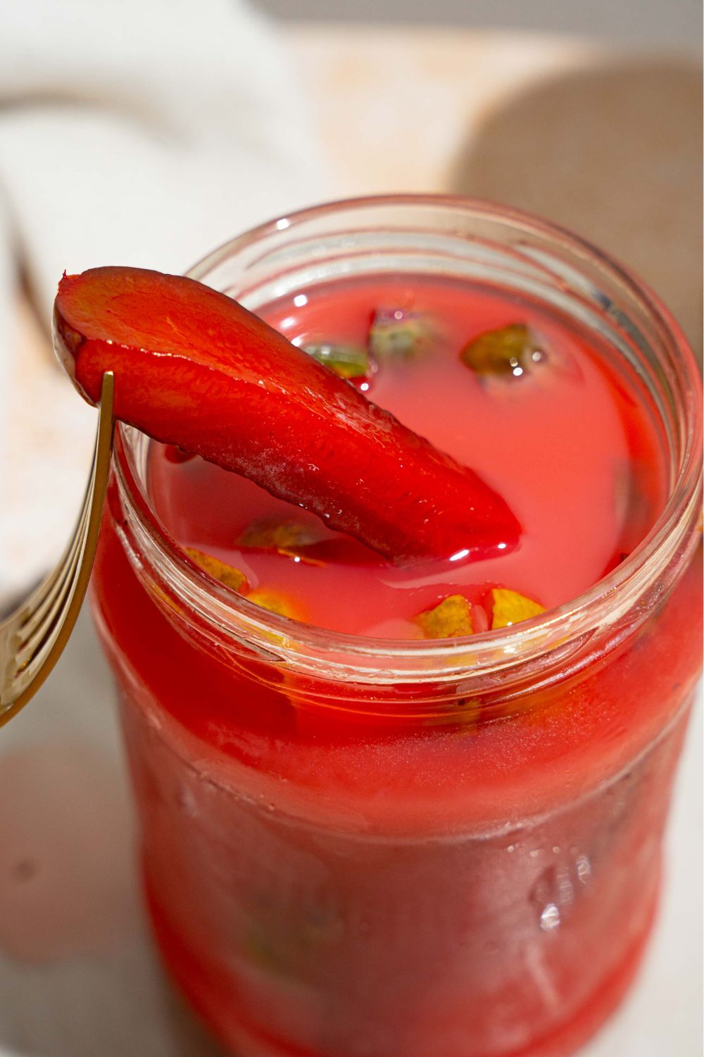 A jar of kool aid pickles with a pickle leaning out of the jar. The jar is on a tan counter.