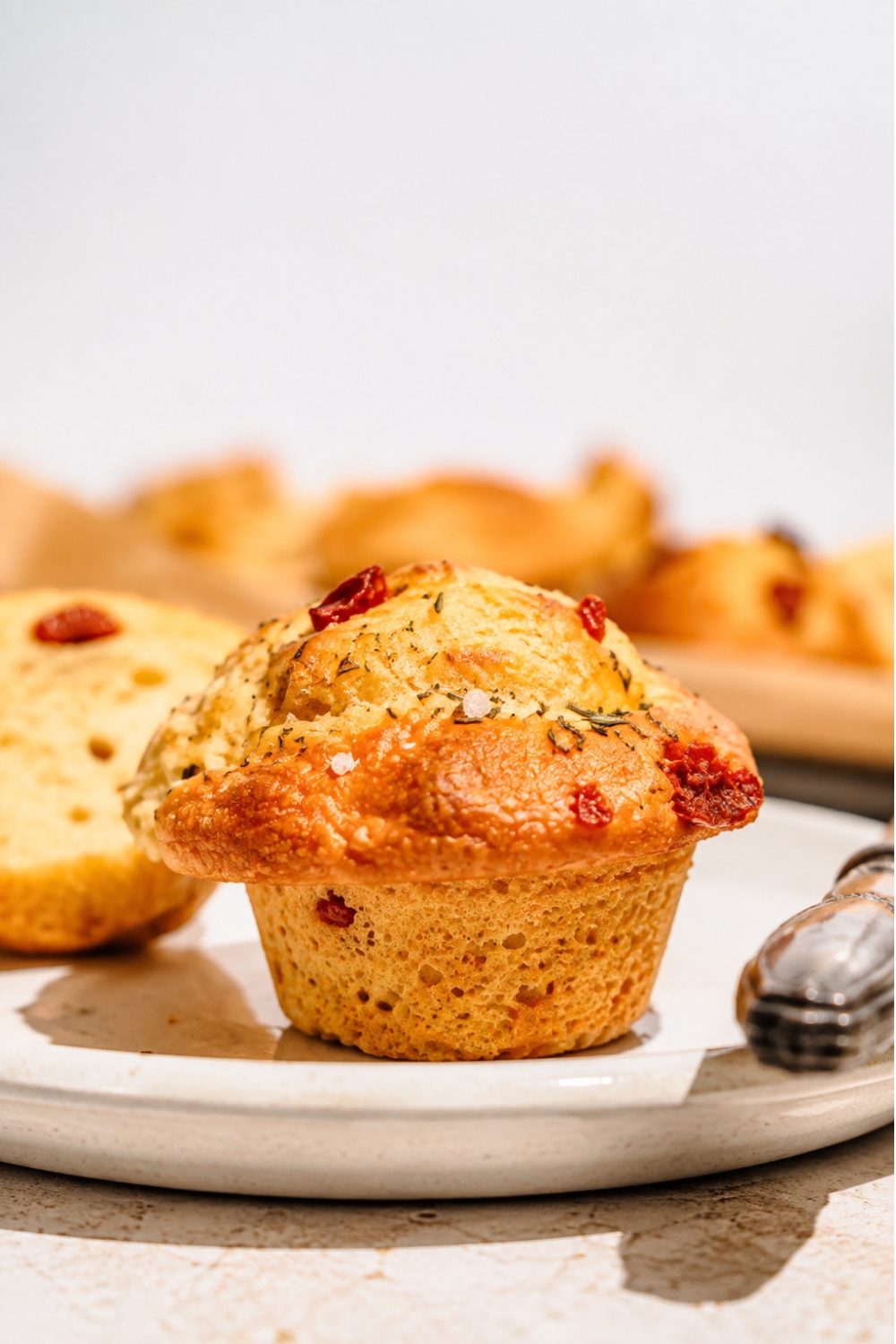 A white plate with rosemarry focaccia muffins with a knife on the plate. The plate is on a tan counter with a tray of muffins.