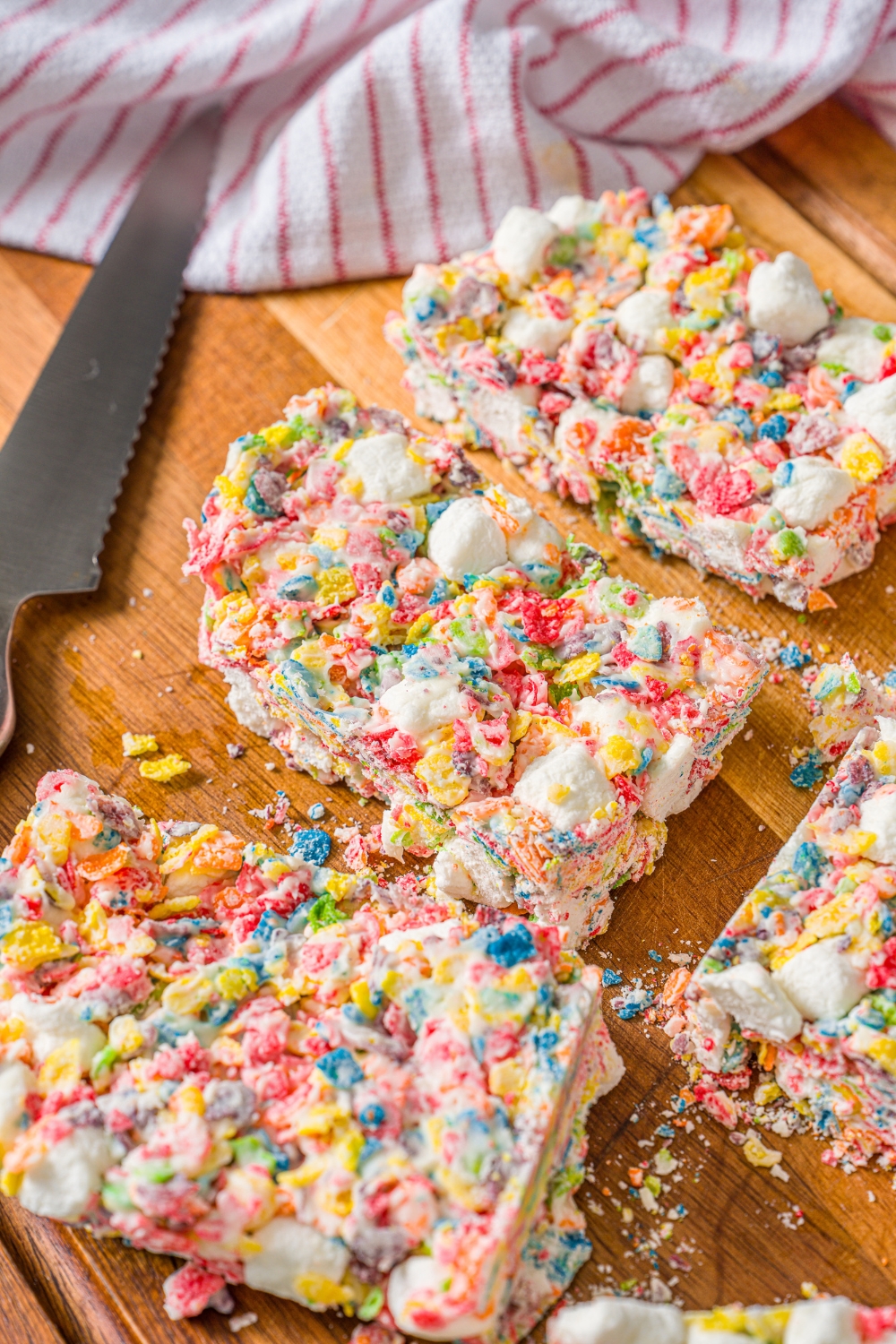 A wooden board with sliced fruity pebbles rice crispy treats and a knife.