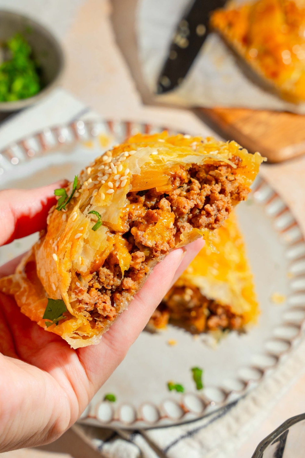 A close up of a hand holding a cheeseburger hot pocket sliced in half. There is a plate with the remaining hot pocket blurred in the background.