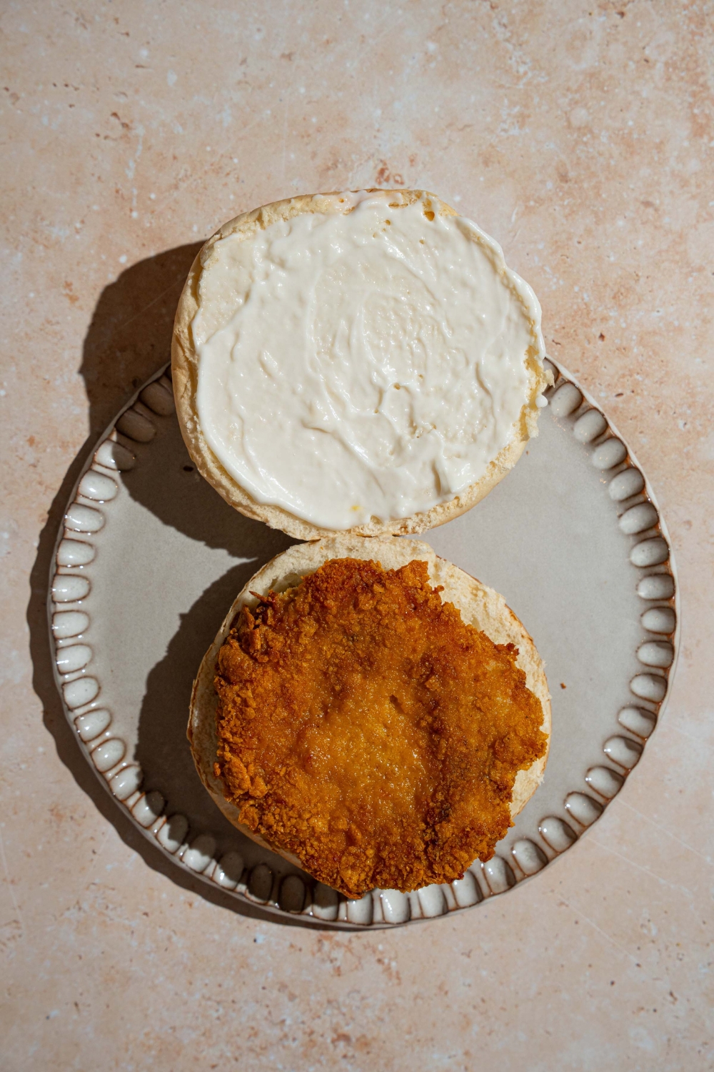 A plate with an open McChicken sandwich with mayo spread on the top bun. The plate is on a tan counter.